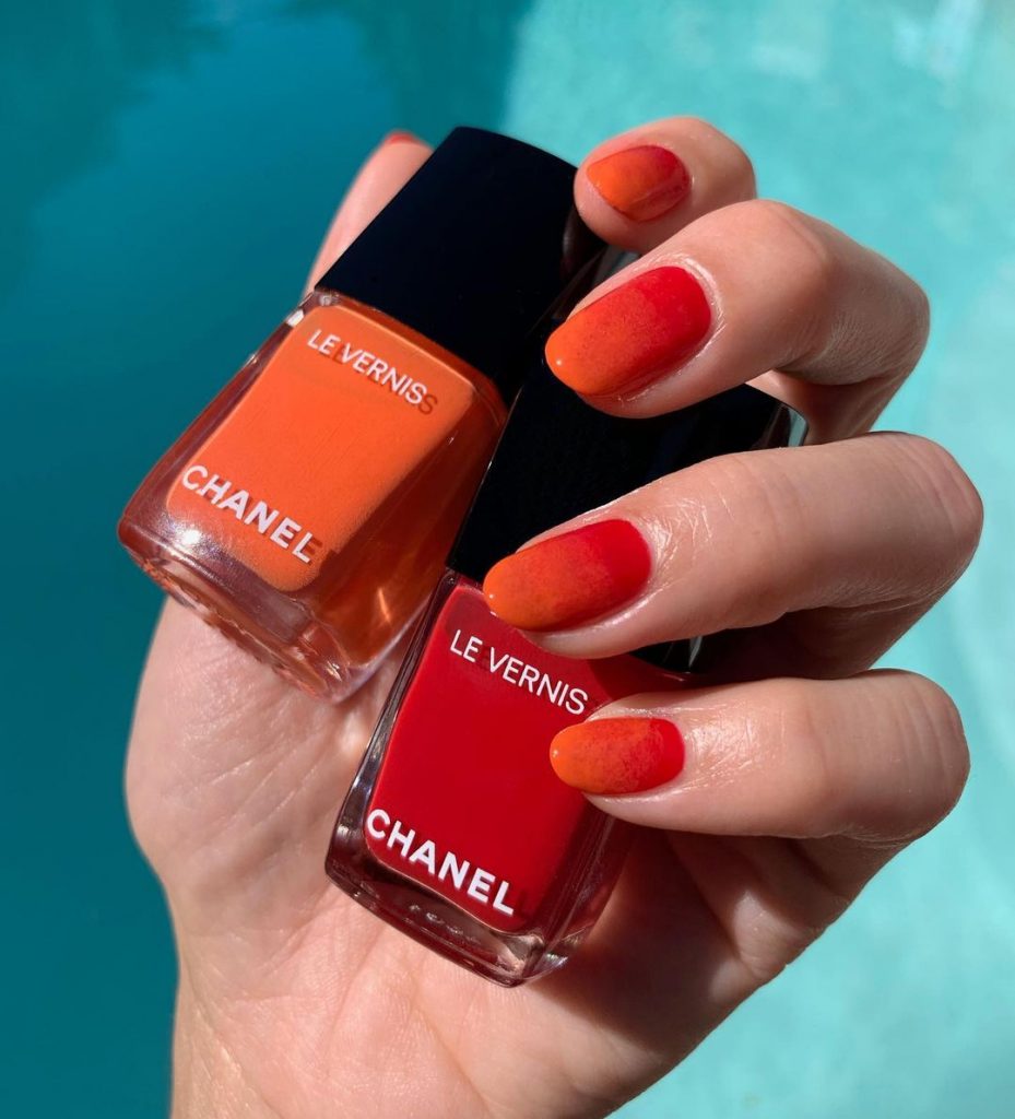 Two Chanel nail art bottles in red and orange held my manicured hand with matching orange fingernails