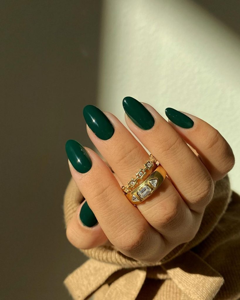 Deep Green fingernails on a womans hand with gold and diamond rings