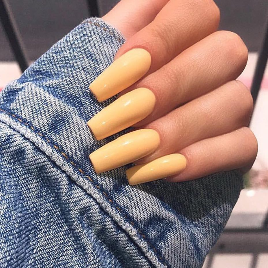 long yellow fingernails on a womans hand showing from denim sleeve