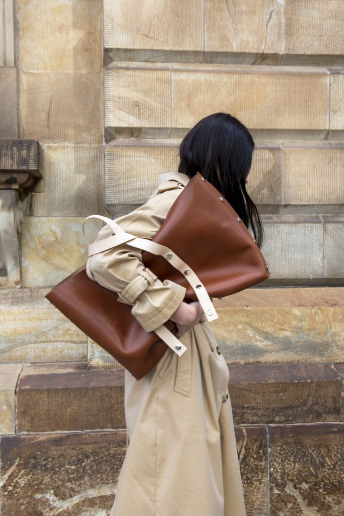large leather bag carried by woman in trench coat under her arm