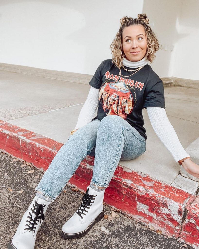 Blong curly haired woman sitting on kerb wearing tee over turtleneck and denim jeans