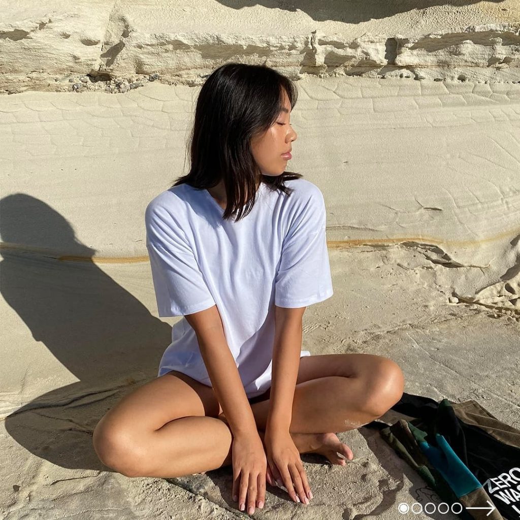 Girl sitting on beach wearing a sustainable white tee by Citizen Wolf